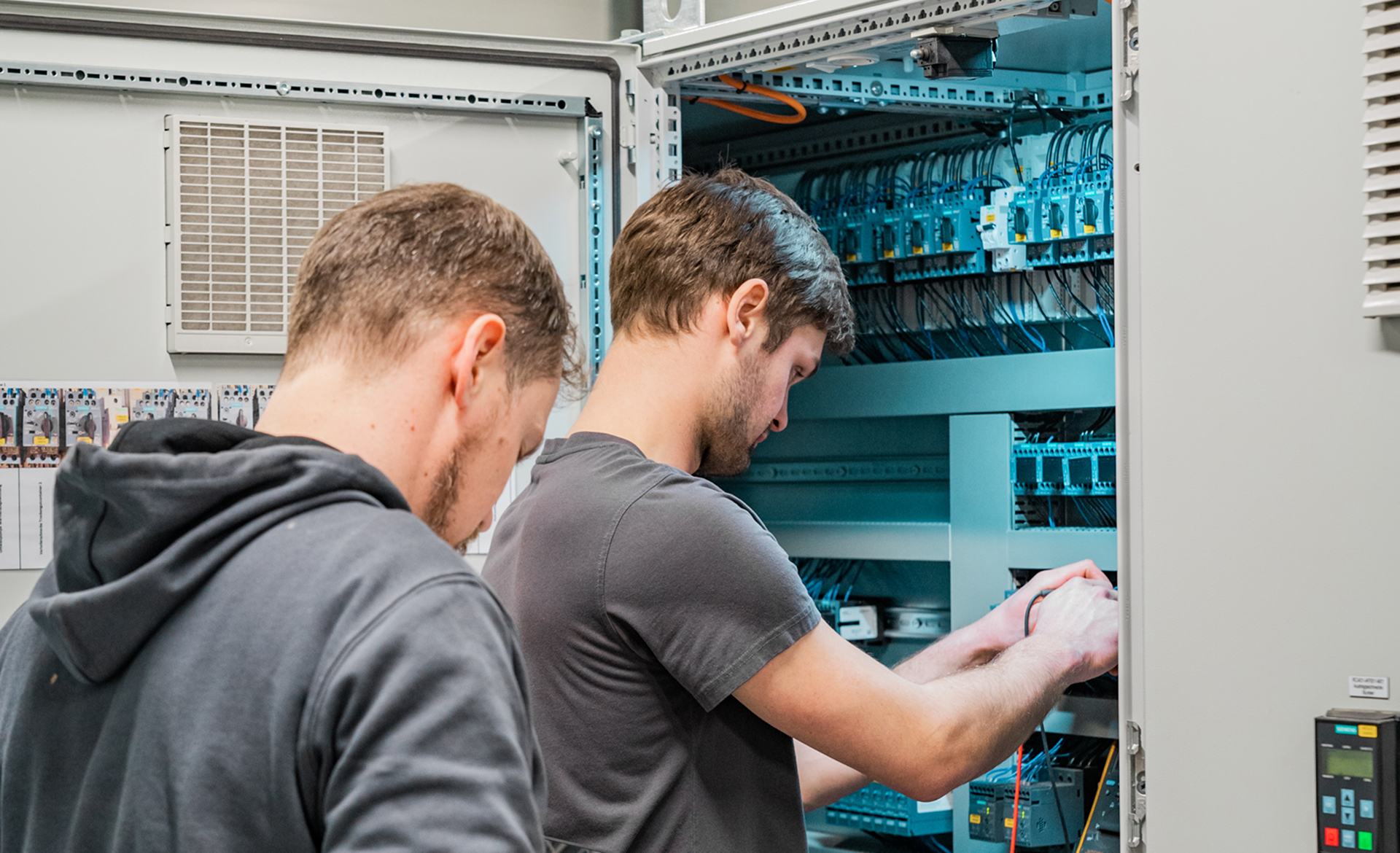 Zwei Techniker arbeiten an einem Schaltschrank, während sie elektrische Verbindungen überprüfen und installieren.