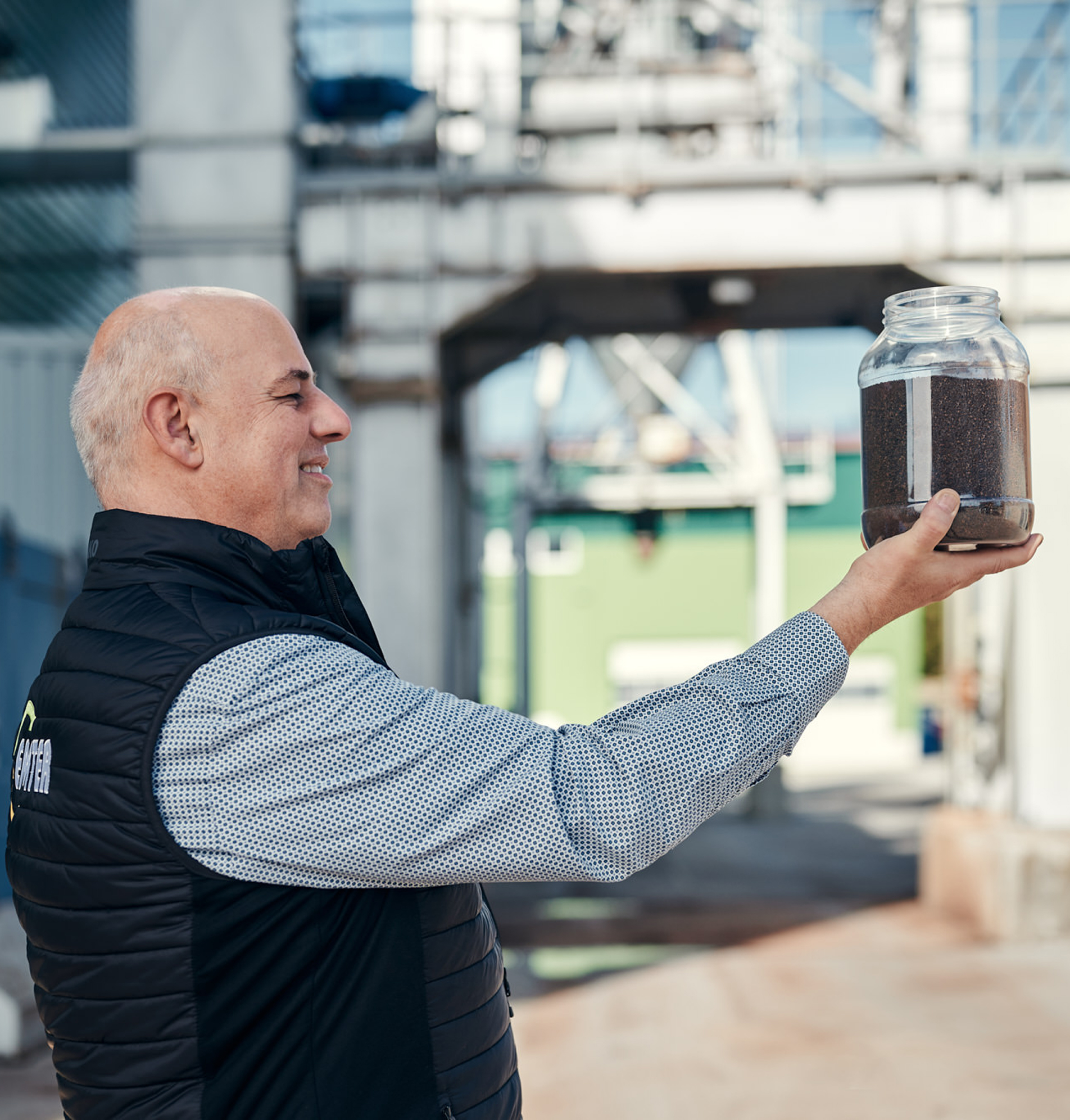 Ein Mitarbeiter von Emter hält ein Glas mit dunklem Phosphor in einer industriellen Umgebung.