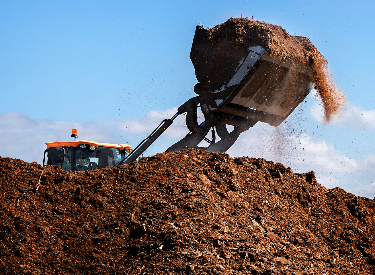 Traktor kippt Erde auf einen Haufen, während Staub und Schmutz in die Luft wirbeln, unter klarem Himmel.