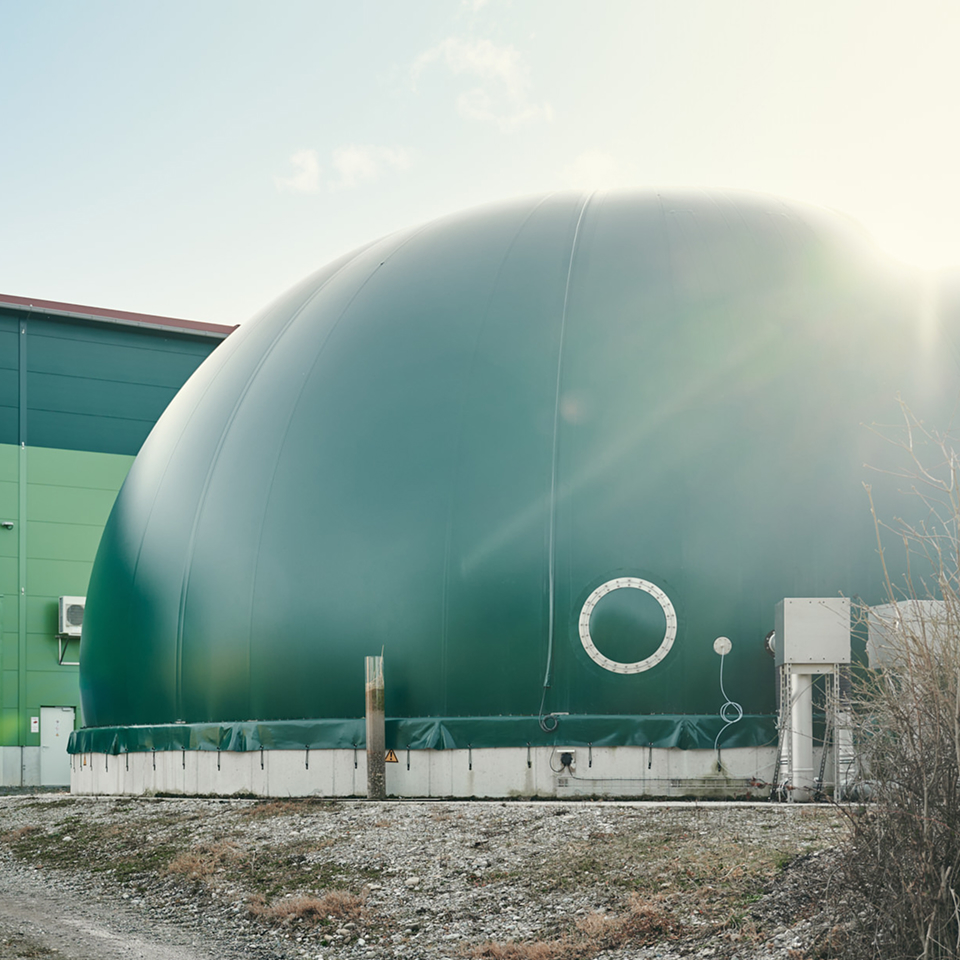 Grüne Biogasanlage mit rundem Tank und angrenzendem Gebäude, umweltfreundliche Energieproduktion im Fokus.