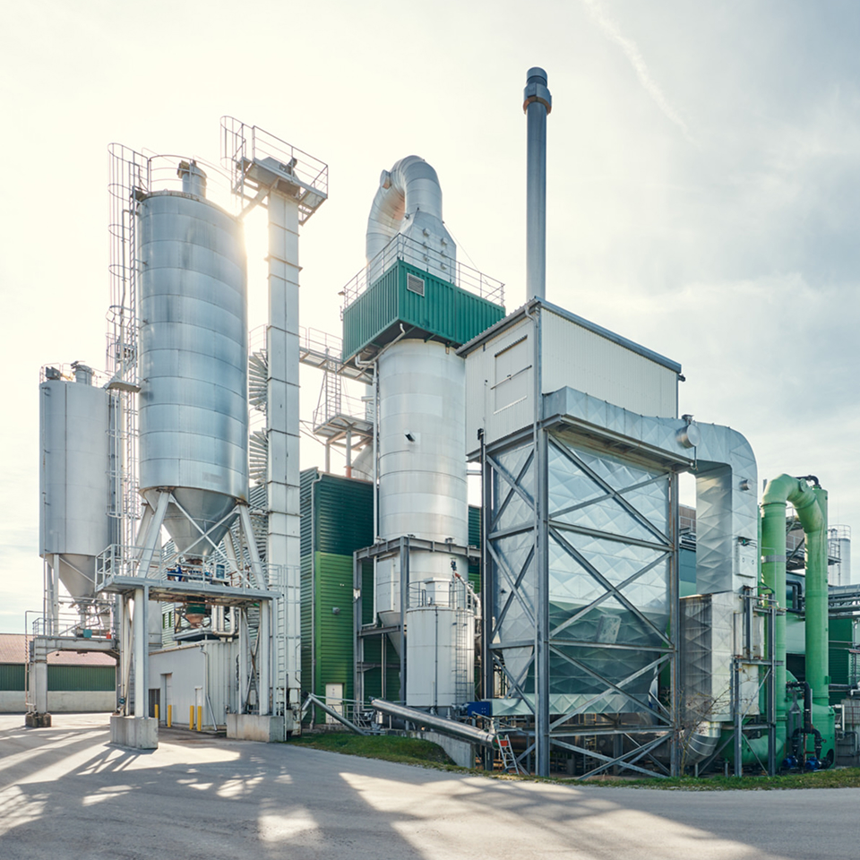 Moderne Industrieanlage mit silbernen Silos und grünen Elementen, umgeben von einem klaren Himmel.